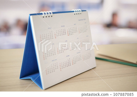 White paper desk calendar on wood table top with blurred office interior background appointment and business meeting concept 107887085