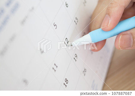 Hand with pen writing on calendar date 107887087