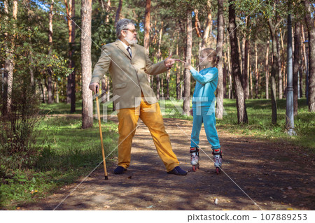 Grandfather walks with his granddaughter in the park. 107889253