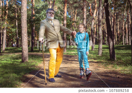 Grandfather walks with his granddaughter in the park. 107889258