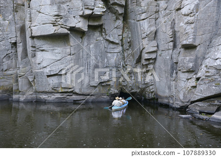 Canoe with people aboard going inside of a cave of rocks. Buksky canyon, Ukraine Canoe with people aboard going inside of a cave of rocks. Buksky canyon, Ukraine 107889330