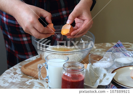 Cook's hand breaking egg into bowl with flour Cook's hand breaking egg into bowl with flour 107889921
