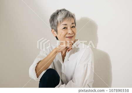 頭髮花白、穿著白襯衫、盤膝坐的優雅日本女子。 頭髮花白、穿著白襯衫、盤膝坐的優雅日本女子。 107890338