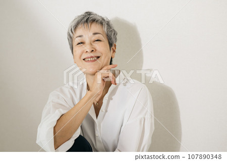 頭髮花白、穿著白襯衫、盤膝坐的優雅日本女子。 頭髮花白、穿著白襯衫、盤膝坐的優雅日本女子。 107890348