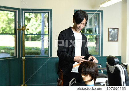 Male hairdresser practicing cutting with a hair mannequin Male hairdresser practicing cutting with a hair mannequin 107890363