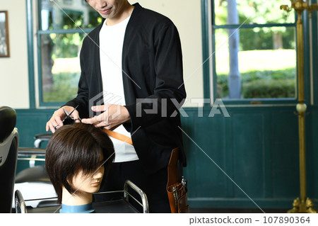 Male hairdresser practicing cutting with a hair mannequin Male hairdresser practicing cutting with a hair mannequin 107890364