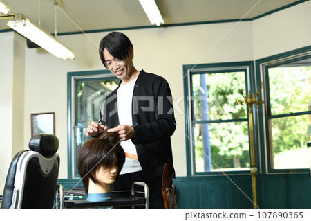 Male hairdresser practicing cutting with a hair mannequin Male hairdresser practicing cutting with a hair mannequin 107890365