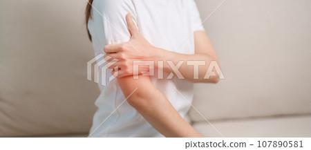 Woman having arm pain during sitting on couch at home, muscle injury and ache. Health and medical concept Woman having arm pain during sitting on couch at home, muscle injury and ache. Health and medical concept 107890581