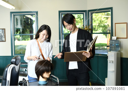 Male and female hairdressers practice cutting with hair mannequins Male and female hairdressers practice cutting with hair mannequins 107891081