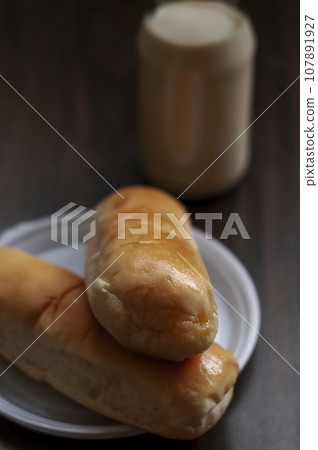 Bread on a white plate sits on a wooden board table with milk in a bottle behind it Bread on a white plate sits on a wooden board table with milk in a bottle behind it 107891927