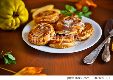 Cooked fried round pancakes with quince filling on a wooden table 107891997
