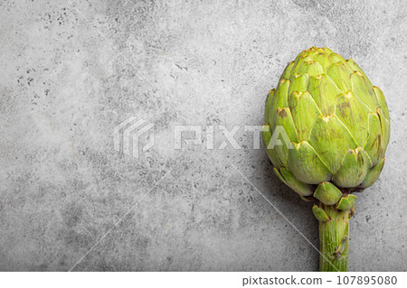 Fresh raw organic farm one artichoke on grey rustic stone background top view, healthy artichokes in balanced nutrition, cooking concept Fresh raw organic farm one artichoke on grey rustic stone background top view, healthy artichokes in balanced nutrition, cooking concept 107895080