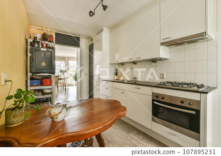 a kitchen with white cabinets and wood table in the middle of the room, there is an oven on the wall a kitchen with white cabinets and wood table in the middle of the room, there is an oven on the wall 107895231
