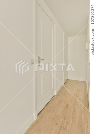 an empty room with white walls and wood flooring on the right side of the room, there is a door leading to another an empty room with white walls and wood flooring on the right side of the room, there is a door leading to another 107895374