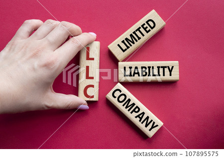 LLC - Limited liability company. Wooden cubes with word LLC. Businessman hand. Beautiful red background. Business and LLC concept. Copy space. 107895575