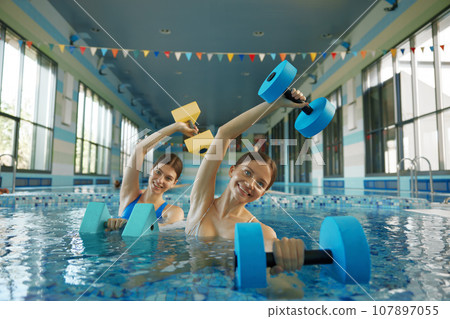 Two beautiful training women enjoying water gymnastics training class at pool Two beautiful training women enjoying water gymnastics training class at pool 107897055