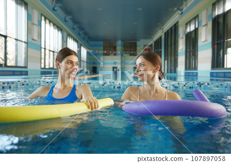 Portrait of female swimmers training with noodles at pool Portrait of female swimmers training with noodles at pool 107897058