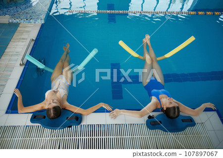 Two women doing relaxing exercise with noodles after training in swimming pool 107897067