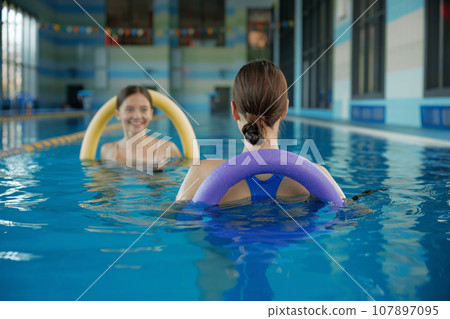 Female fitness class of aqua aerobics at indoors swimming pool Female fitness class of aqua aerobics at indoors swimming pool 107897095
