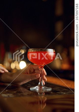 Cocktail drink in female hand over bar counter desk closeup selective focus 107897168