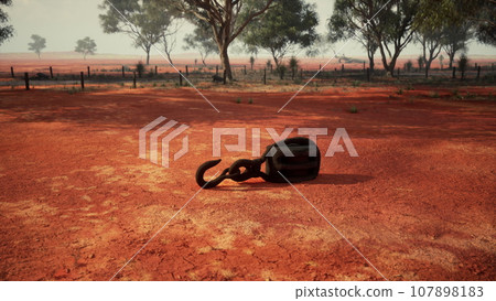 A rusty metal hook on a vibrant red dirt road 107898183