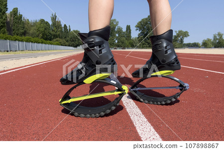Kangoo jump shoes. A girl plays sports in a stadium wearing Kangoo jumping shoes. Kangoo jump shoes. A girl plays sports in a stadium wearing Kangoo jumping shoes. 107898867