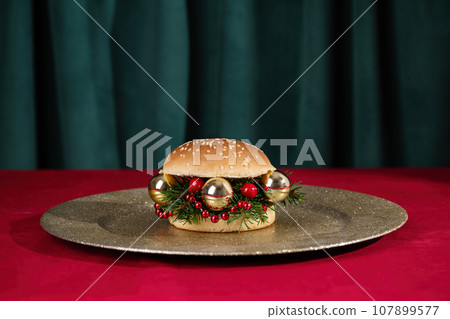 Creative Christmas hamburger. Burger made from fir branches and Christmas ornaments on holiday table. Creative New Year or Christmas food concept. Creative Christmas hamburger. Burger made from fir branches and Christmas ornaments on holiday table. Creative New Year or Christmas food concept. 107899577