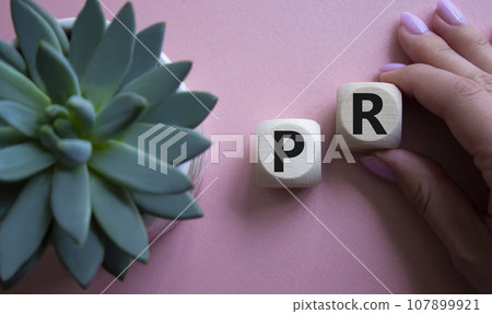 PR - Public Relations symbol. Concept word PR on wooden cubes. Businessman hand. Beautiful pink background with succulent plant. Business and PR concept. Copy space. 107899921