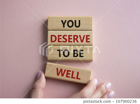 You deserve to be well symbol. Wooden blocks with words You deserve to be well. Beautiful pink background. Businessman hand. You deserve to be well concept. Copy space. 107900236