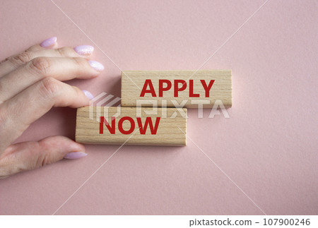 Apply now symbol. Concept word Apply now on wooden blocks. Businessman hand. Beautiful pink background. Business and Apply now concept. Copy space 107900246