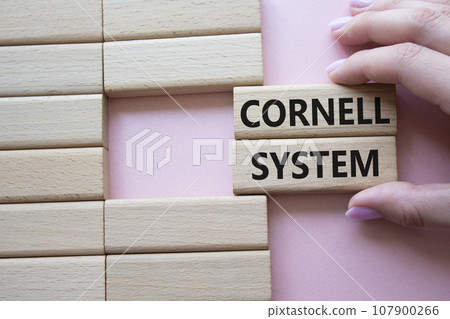 Cornell system symbol. Concept word Cornell system on wooden blocks. Businessman hand. Beautiful pink background. Business and Cornell system concept. Copy space 107900266