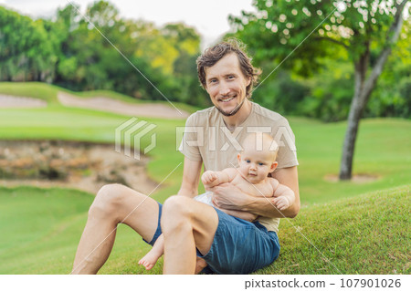 Dad and baby sit on the grass in the park 107901026