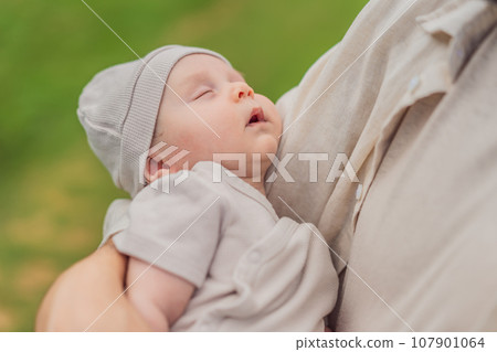 A happy 40-year-old father cradles her newborn in a sun-drenched park. Love, family and generations in harmony 107901064