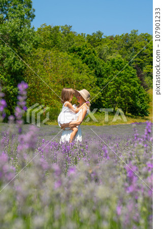 Pretty young woman wearing hat in a lavender field with her young baby daughter Pretty young woman wearing hat in a lavender field with her young baby daughter 107901233