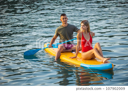 Woman and man surfing in ocean on sup board ar summer vacation. Woman and man surfing in ocean on sup board ar summer vacation. 107902009