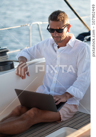 Smiling man in sunglasses spending time online while sailing on a yacht 107902449