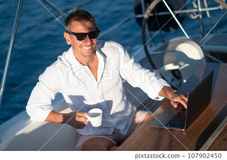 Contented man in sunglasses sitting on a yacht deck with a cup of coffee 107902450