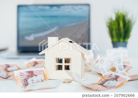 House model with British currency and sea beach view on laptop screen. Concept of dream of real estate on the beach. Property investment. Home mortgage loan rate. Saving money for retirement concept. 107902666