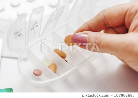 Woman hand putting pills into open pill organizer or plastic pillbox 107902693