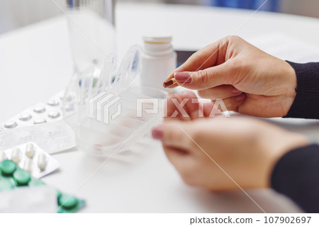 Woman hand putting pills into open pill organizer or plastic pillbox 107902697