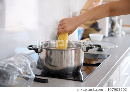 Close-up housewife's hand taking off spaghetti from a container while cooking dinner in the home kitchen 107903302