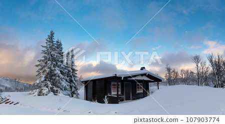 A small snow covered hunting lodge in the norwegian mountains with animal traces in the foreground and mountain summits in the background A small snow covered hunting lodge in the norwegian mountains with animal traces in the foreground and mountain summits in the background 107903774
