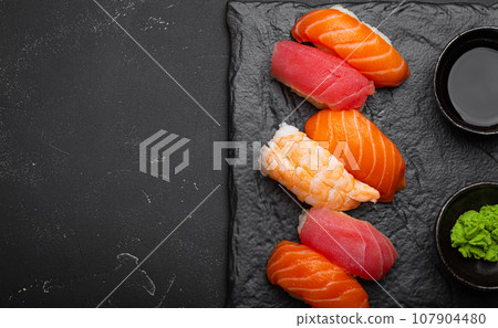 Traditional Japanese sushi with soy sauce, wasabi, chopsticks top view on dark black rustic slate. Sushi with salmon, tuna, shrimp, space for text Traditional Japanese sushi with soy sauce, wasabi, chopsticks top view on dark black rustic slate. Sushi with salmon, tuna, shrimp, space for text 107904480
