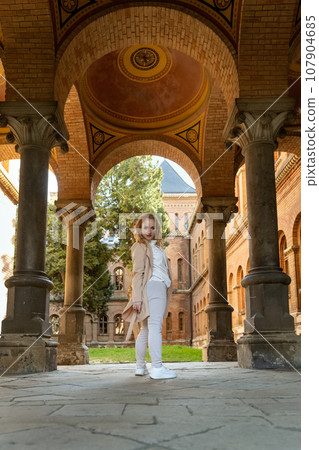 Young woman posing for photo in the arch of historic building. Full-length portrait of girl looking over her shoulder. Young woman posing for photo in the arch of historic building. Full-length portrait of girl looking over her shoulder. 107904685