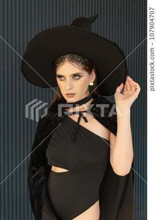 Sexy woman wearing in black witch hat and black bodysuit. Girl with seductive look. . Beautiful makeup. Halloween Outfit Sexy woman wearing in black witch hat and black bodysuit. Girl with seductive look. . Beautiful makeup. Halloween Outfit 107904707
