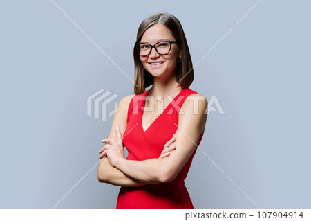 Young confident woman in glasses with crossed arms on grey background 107904914