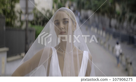 Portrait of a beautiful and attractive bride with blonde hair. Action. Close up of the face of a young woman in a wedding veil with make up. Portrait of a beautiful and attractive bride with blonde hair. Action. Close up of the face of a young woman in a wedding veil with make up. 107906275
