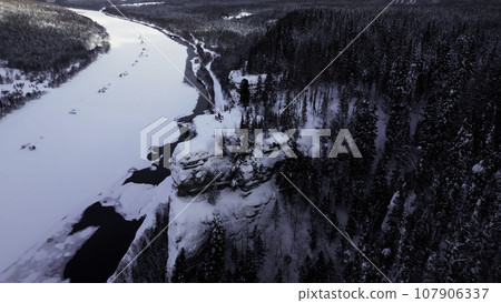 Cinematic aerial epic scene of group of skiers and hikers on top of a mountain. Clip. Winter at the cliff peak on the background of frozen river, forest and cloudy sky. Cinematic aerial epic scene of group of skiers and hikers on top of a mountain. Clip. Winter at the cliff peak on the background of frozen river, forest and cloudy sky. 107906337