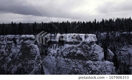 Aerial winter snow scene with ice covered cliff. Clip. White cliff edge with forested top. 107906353