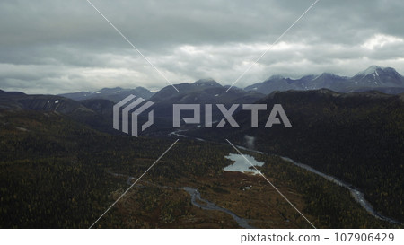 Aerial flight over amazing small lake surrounded by forested valley and mountains. Clip. Untouched nature from above on late autumn day. 107906429